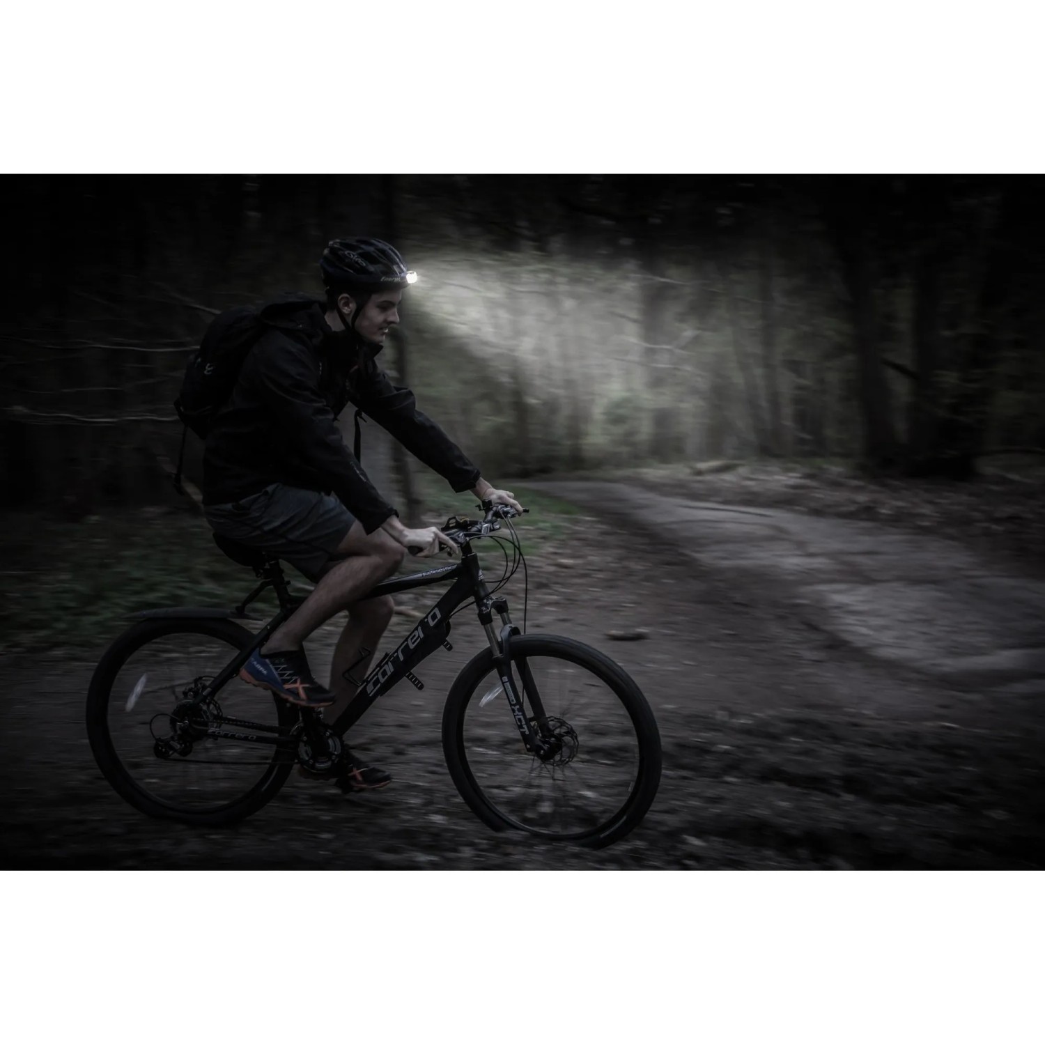 Mann fährt mit dem Fahrrad im Dunkeln, mit Energizer Kopflampe Compact Sport Headlamp.