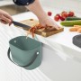 Rotho Bio-Mülleimer Albula in Mistletoe Green, hängend an einer Küchentür, mit Deckel und Gemüseresten.