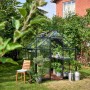 Schwarzes Halls Gewächshaus Qube 68 (5 m²) im Garten mit Pflanzen und Stuhl.