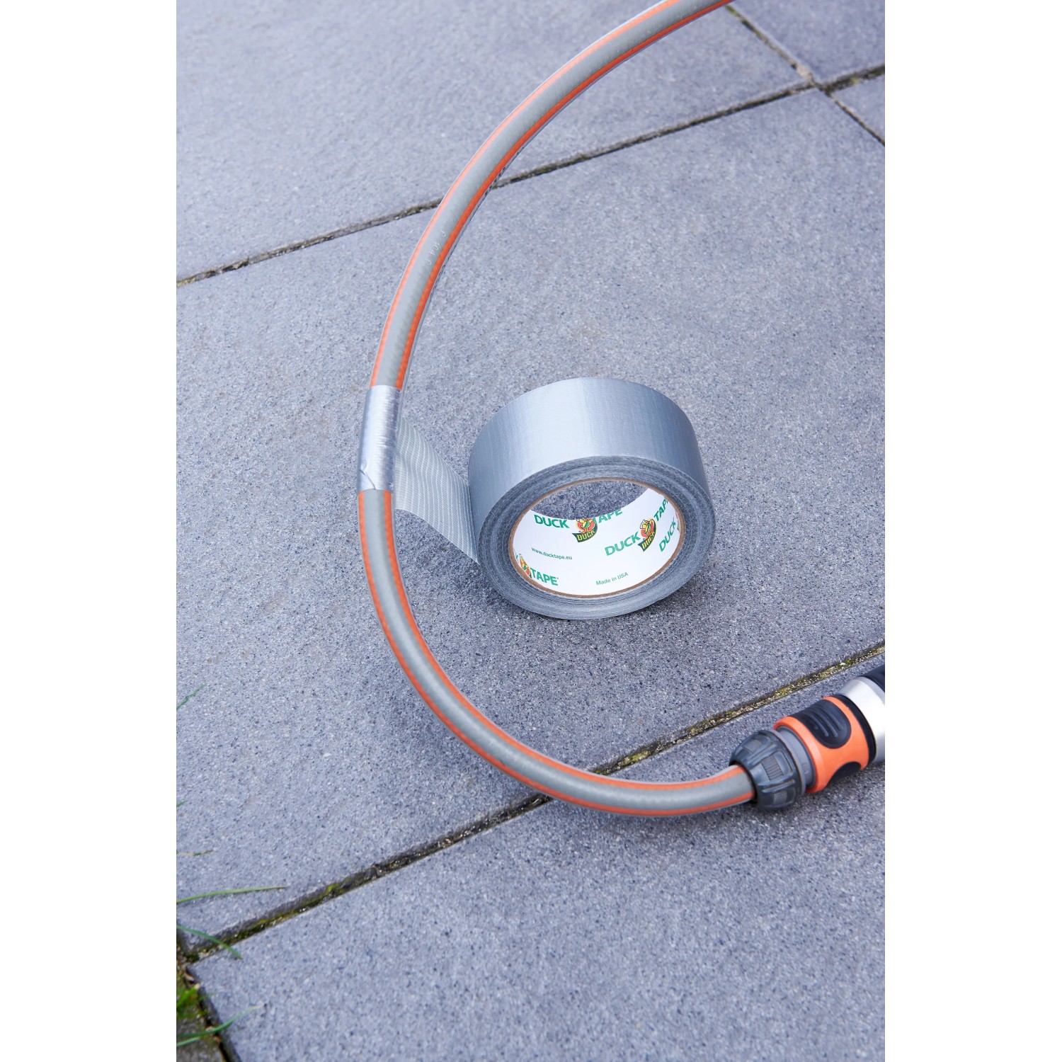 Silbernes Duck Tape Gewebe-Klebeband repariert einen Gartenschlauch auf Pflastersteinen.