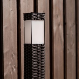 Schwarze Solar-Wegeleuchte Muscat mit Sensor und warmweißem Licht vor Holzwand.