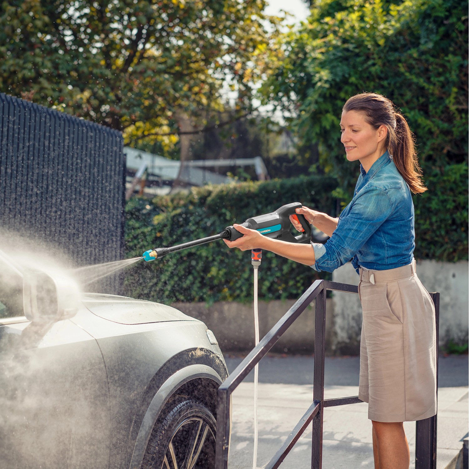 Frau reinigt Auto mit Gardena Akku-Mitteldruckreiniger AquaClean 24/18V. Hochdruckreiniger im Einsatz.