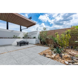 Graue, strukturierte Bagattini Terrassenplatten Rustica Perla auf einer modernen Terrasse mit Feuerstelle und Pflanzen.