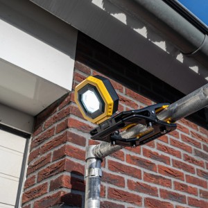 Gelb-schwarze LED-Akku-Arbeitsleuchte mit Klemme an einem Rohr befestigt.