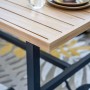 Detail des Elati Gartenmöbel Tisches: Teak-Look-Platte, dunkles Aluminiumgestell, Geschirr auf gemustertem Teppich.
