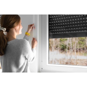 Frau befestigt weißen Schellenberg Rollladengurt Maxi (23mm, 6m) am Fenster.