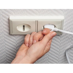 Hand steckt Eurostecker in weiße Steckdose. Euro-Steckdosenleiste für Innenräume.