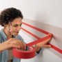 Frau klebt rotes tesa® Malerband Excellent an Wand für präzise Farbkanten.