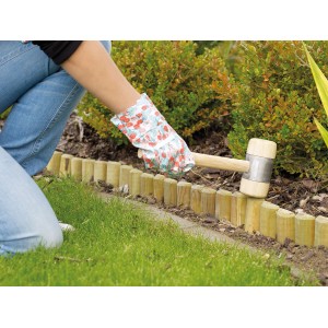 Beeteinfassung aus Holz wird mit Gummihammer im Garten fixiert.