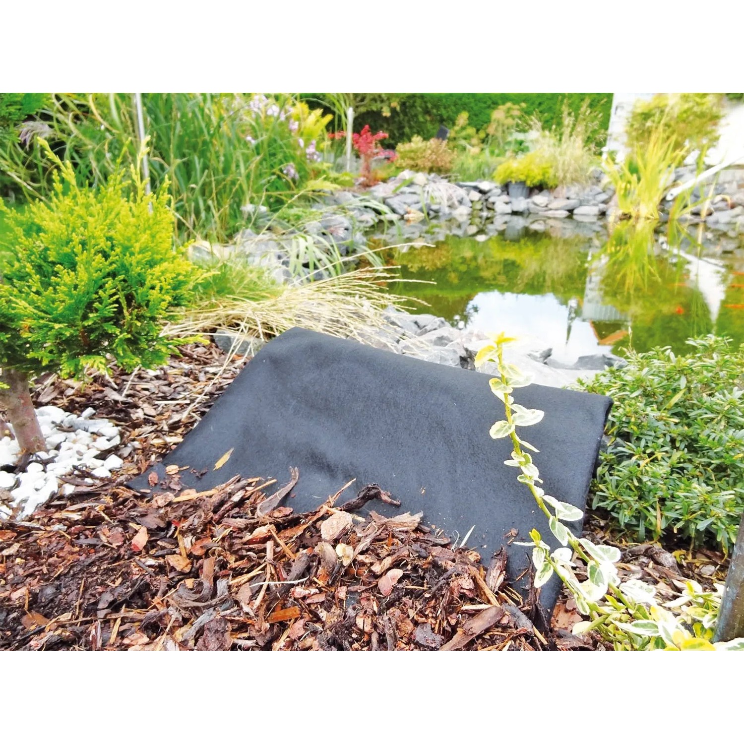 Heissner Unkrautvlies, 1m breit, im Gartenbeet vor einem Teich. Bodenabdeckung für Unkrautschutz.