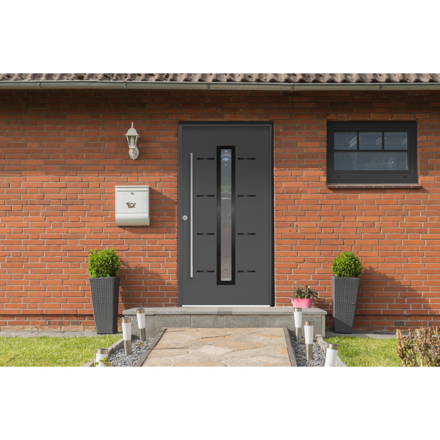 Moderne, anthrazitfarbene Sicherheits-Haustür mit Glaseinsatz und Edelstahlgriff in Backsteinhaus-Fassade.