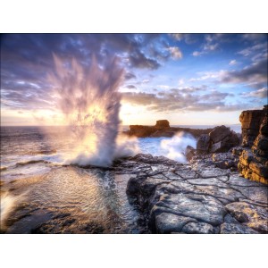Leinwandbild Elemente, 84x116 cm: Gischtfontäne an felsiger Küste im warmen Licht.