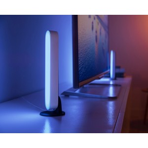 Philips Hue Play LED-Tischleuchte, Weiß, mit farbiger Ambiente-Beleuchtung neben einem Fernseher.