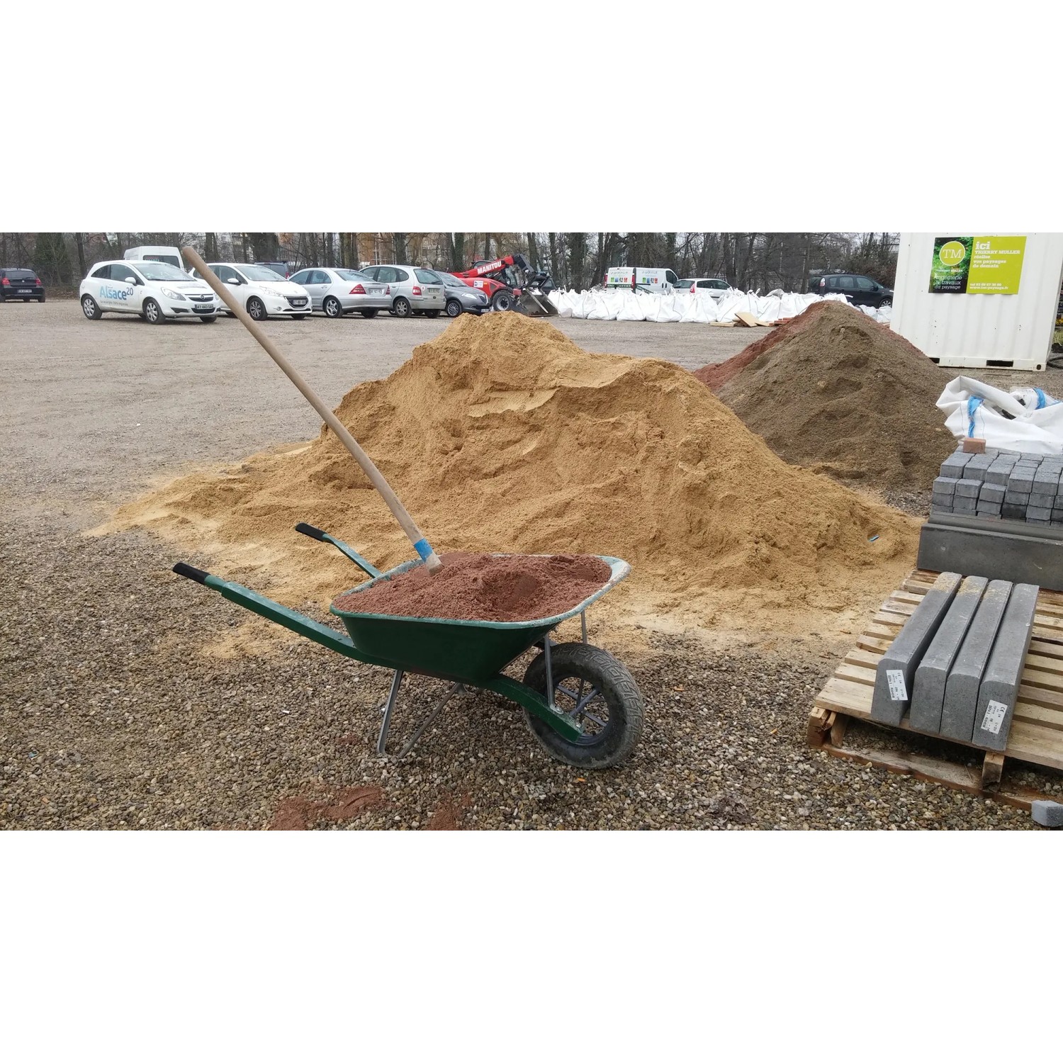 Haemmerlin Schubkarre Pro Select 90 l verstärkt mit roter Erde und Schaufel vor Sandhaufen.