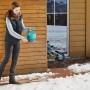 Frau streut mit Gardena Handstreuer M Streusalz auf vereister Fläche.