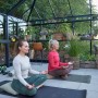 Zwei Frauen machen Yoga im Juliana Gewächshaus Grand Oase 25 Schwarz-Anthrazit, umgeben von Pflanzen.