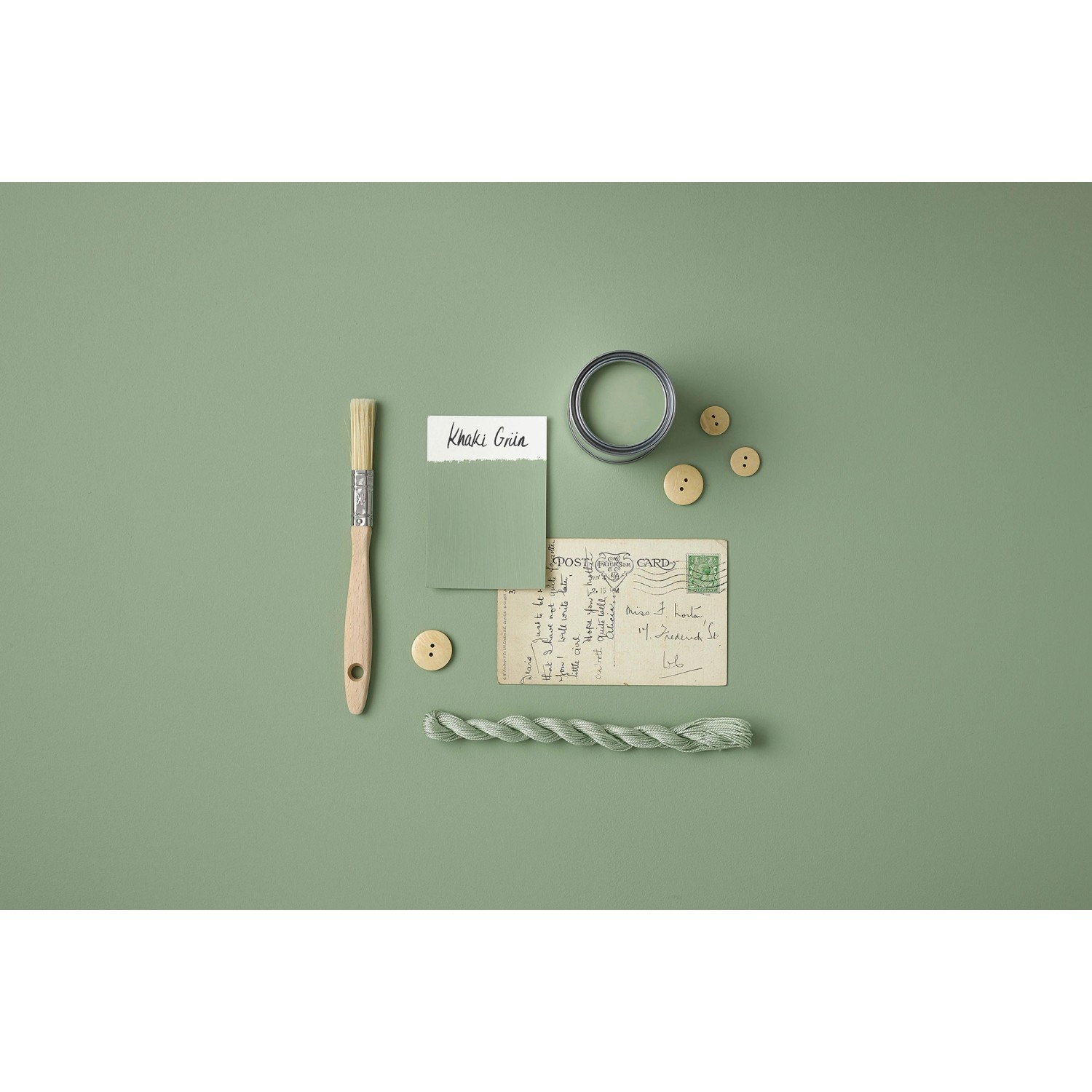 Rust-Oleum Kreidefarbe Khaki Grün matt, mit Pinsel, Knöpfen und Postkarte auf farbigem Untergrund.
