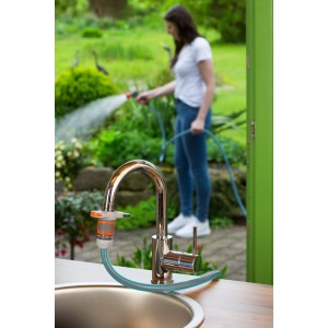 Gardena Indoor Set mit Brause am Wasserhahn, Frau gießt Pflanzen im Hintergrund.