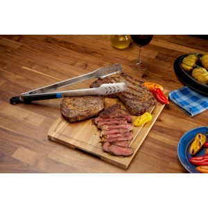 Napoleon Grillzange Essential aus Edelstahl auf Holzbrett mit gegrilltem Steak und Paprika. Strukturierte Greifflächen, Feststellmechanismus.