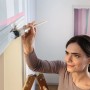 Frau streicht Wand mit Tesa Malerband Professional Sensitive für empfindliche Oberflächen.