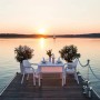 Szene mit weißen Lechuza Essstühlen am See bei Sonnenuntergang. Gartenstühle mit Tisch und Dekoration.