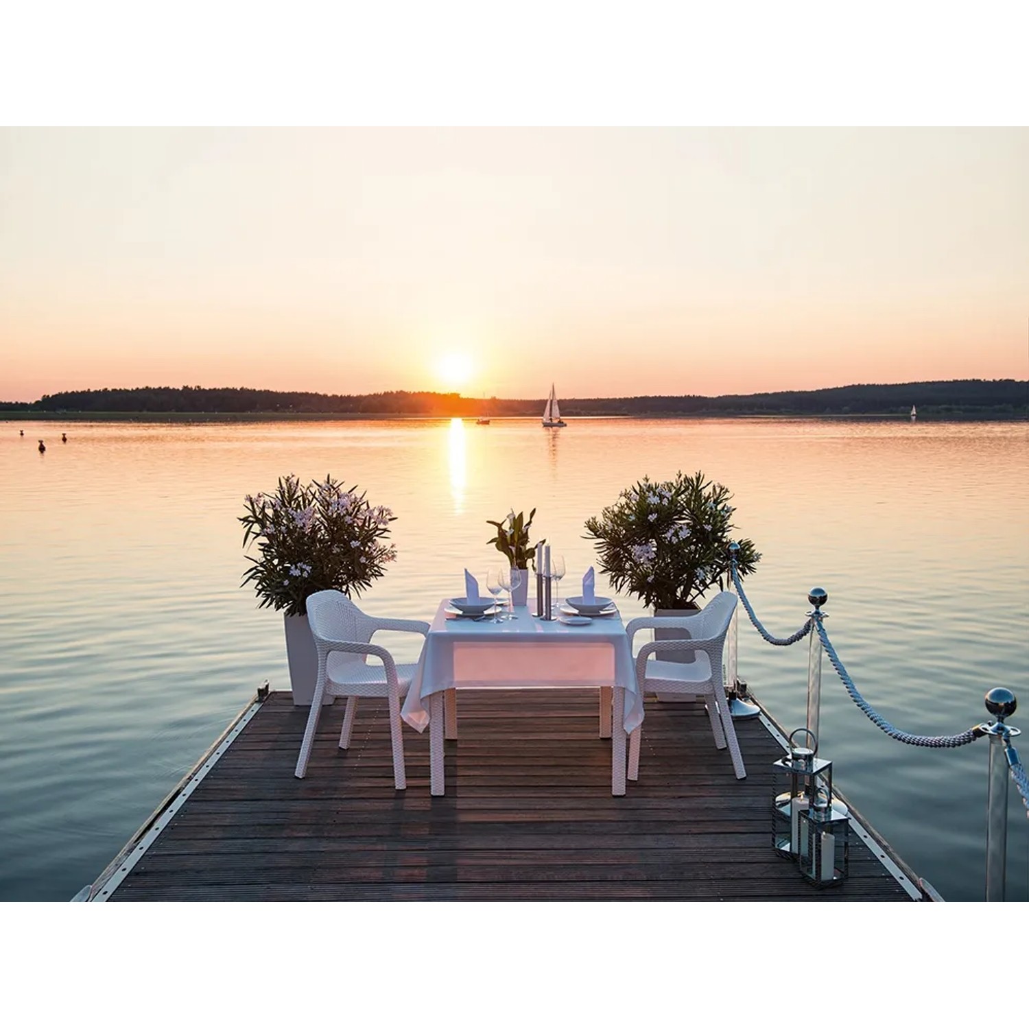 Szene mit weißen Lechuza Essstühlen am See bei Sonnenuntergang. Gartenstühle mit Tisch und Dekoration.