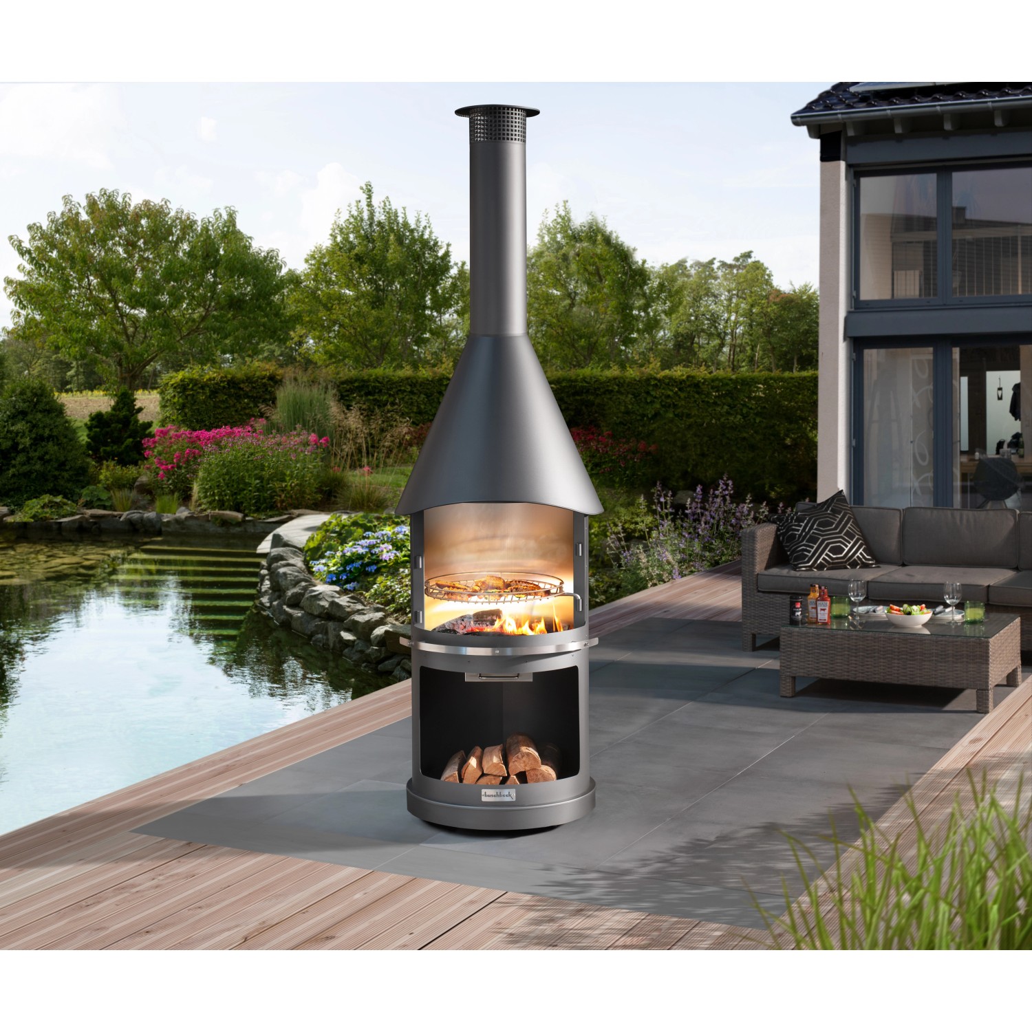 Buschbeck Gartengrillkamin Sydney Dunkelgrau mit Grillrost und Holz im Brennraum.