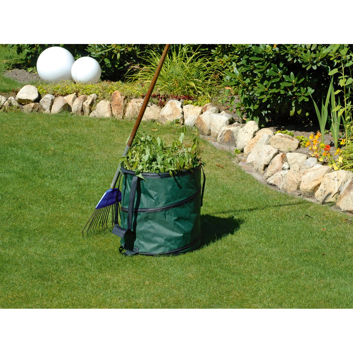 Grüner Gartensack Pop-Up (85 l) mit Gartenabfällen und Rechen im Garten.
