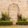 Feuerverzinkter Eleo Rosenbogen Matera (235 cm) mit Kletterpflanzen vor Steinmauer.