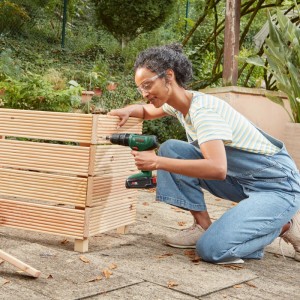 Frau montiert Hochbeet mit Bosch Akku-Schlagbohrschrauber EasyImpact 18V-40 im Garten.