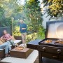Char-Broil Versa-Tile Gasgrill mit Grillfläche, Pizzaaufsatz und entspannten Menschen im Garten.