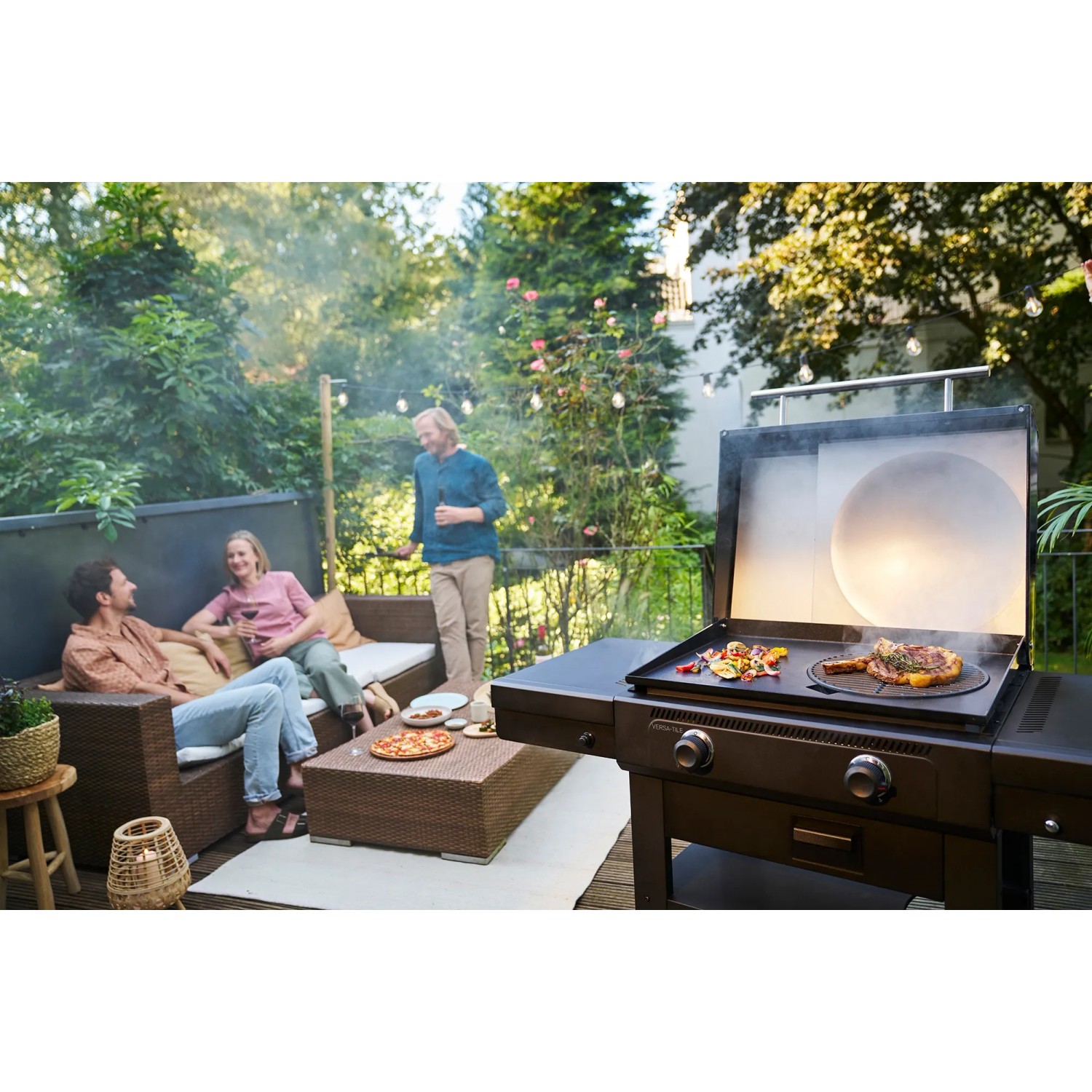 Char-Broil Versa-Tile Gasgrill mit Grillfläche, Pizzaaufsatz und entspannten Menschen im Garten.