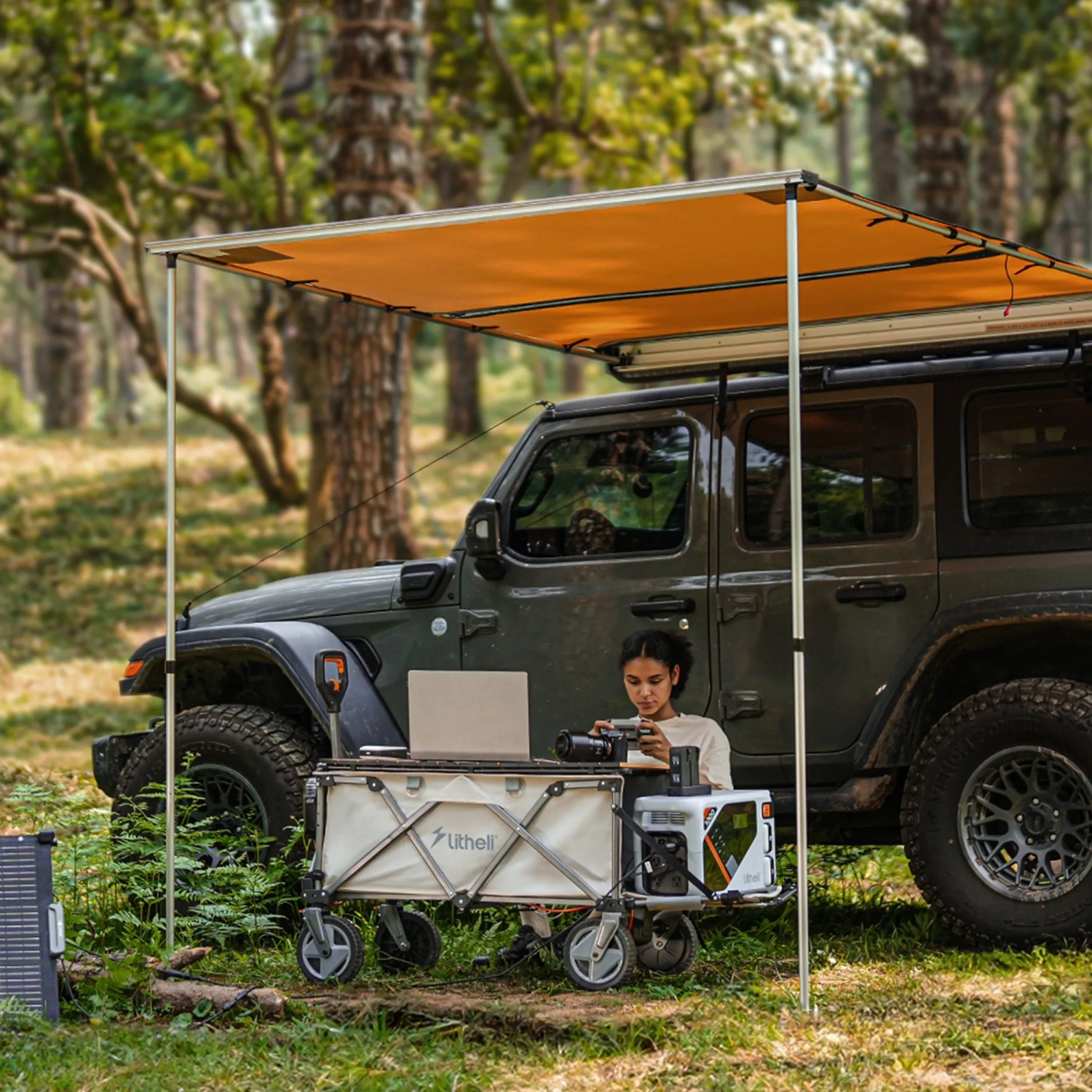 Litheli Bollerwagen W1 Pro mit Akku als Campingtisch mit Laptop und Kamera vor Jeep.