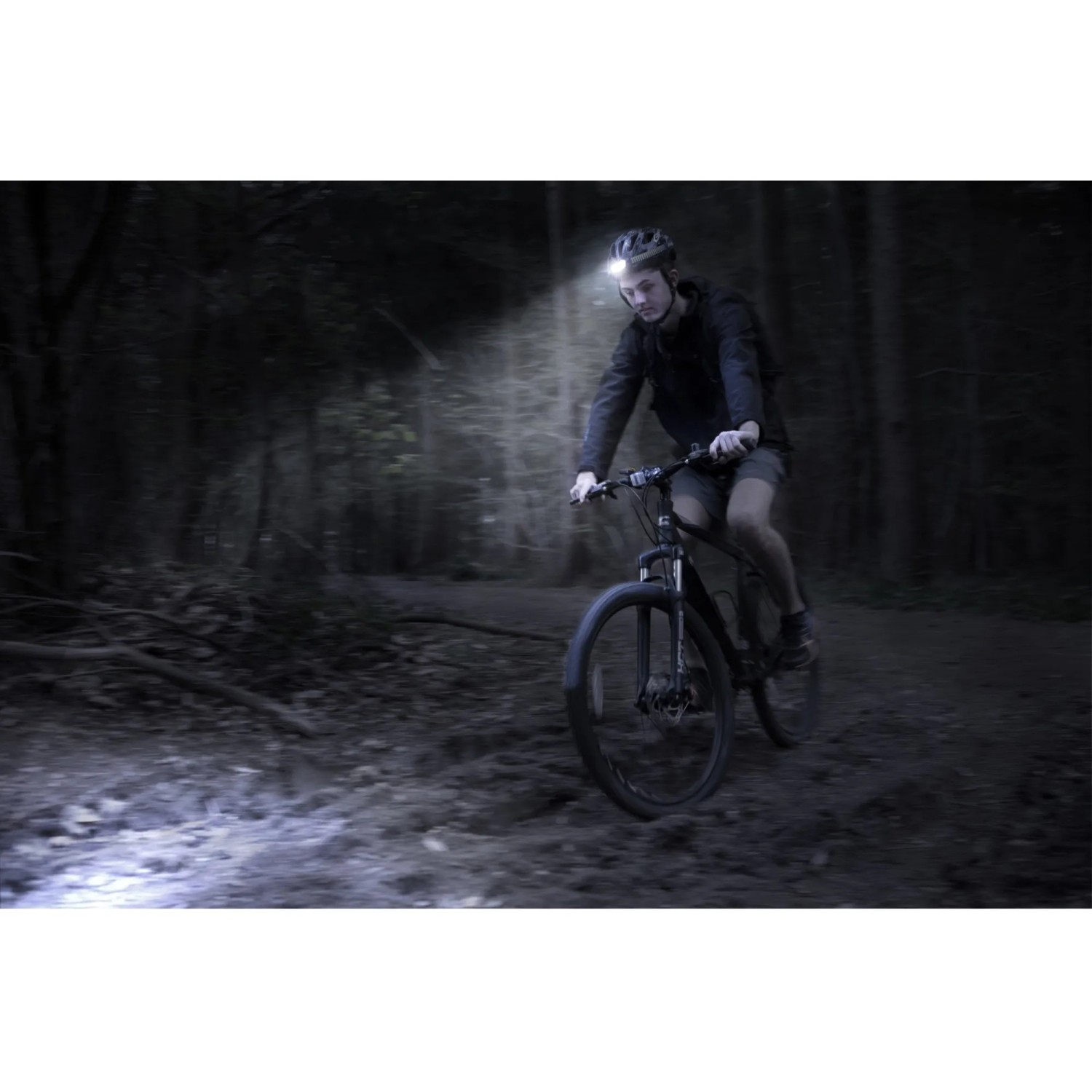 Mann fährt mit Mountainbike im Wald, trägt Energizer Kopflampe Compact Sport Headlamp.