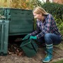 Frau befüllt grünen Garantia Thermo-King Komposter 400 l im Garten.