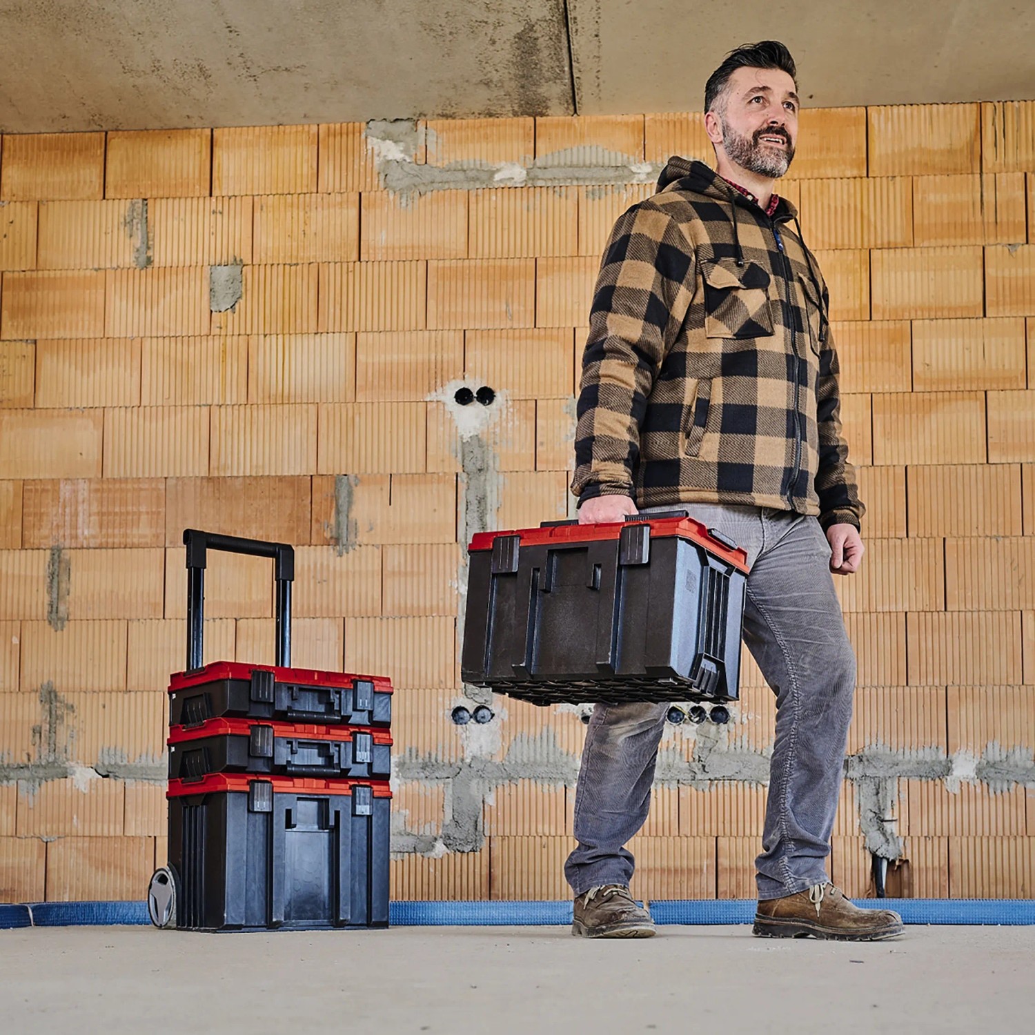 Einhell E-Case M Systemkoffer mit Träger und gestapelten Koffern im Rohbau.