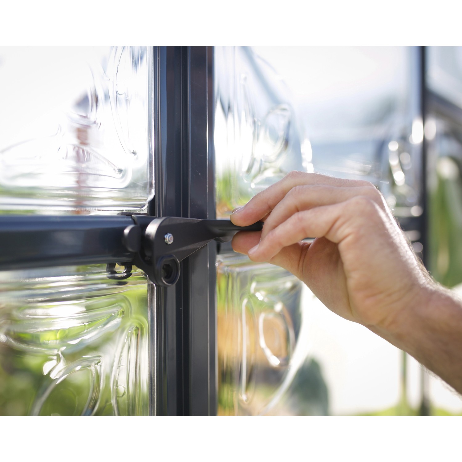 Detailaufnahme: Hand öffnet Fenster des Palram Canopia Victory Orangerie Gewächshauses.