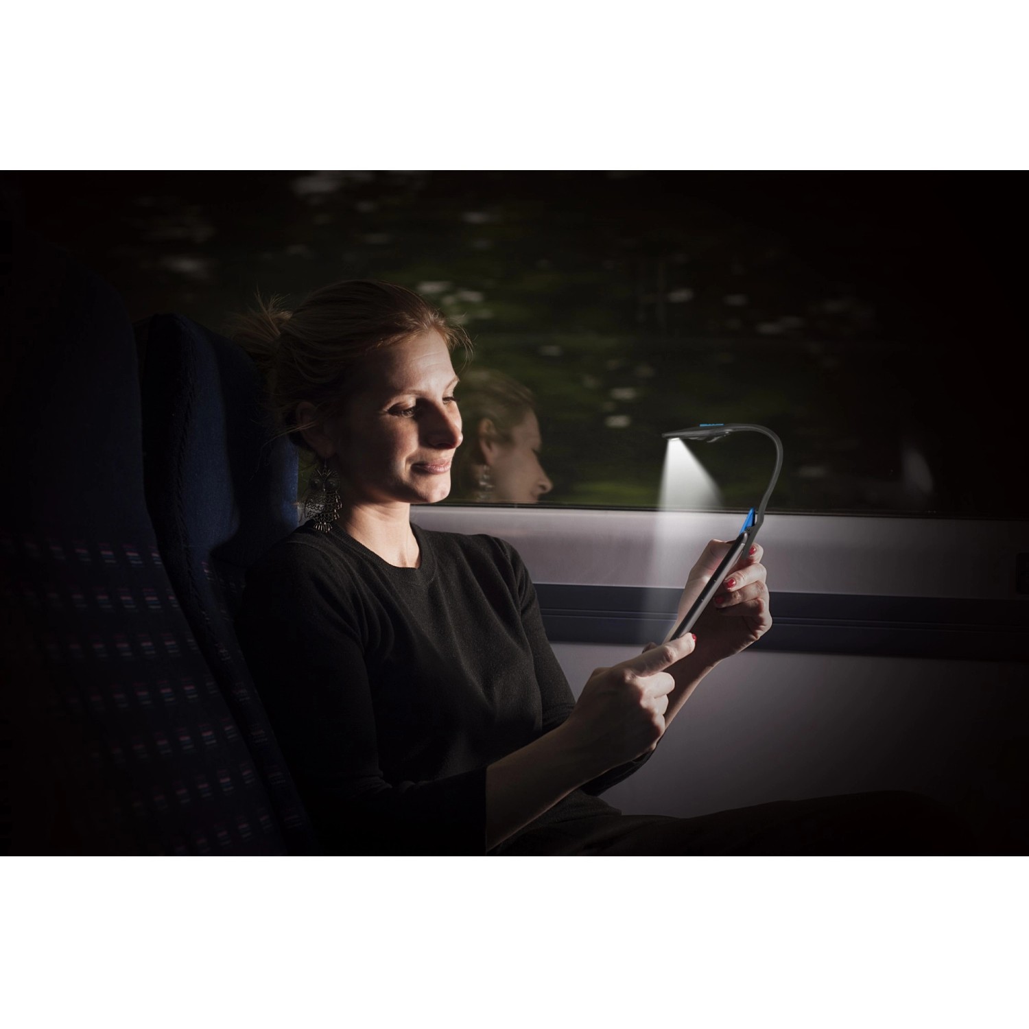 Frau liest mit Energizer Booklight Speziallampe im Zug. Flexible LED-Taschenlampe mit Klemme.