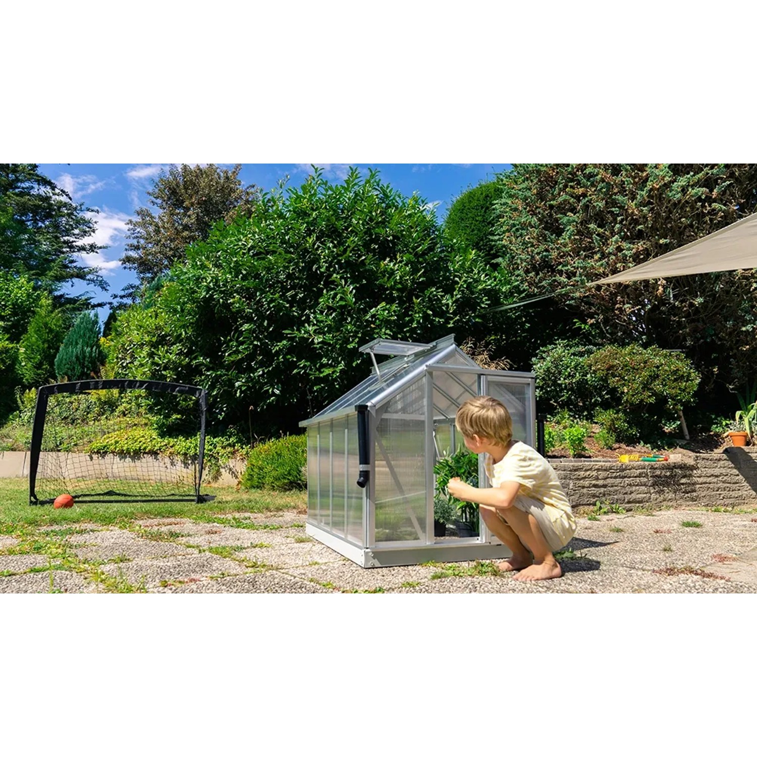 Vitavia Minigewächshaus Merlin mit Kind im Garten. Kleines Gewächshaus aus Aluminium mit Hohlkammerplatten.