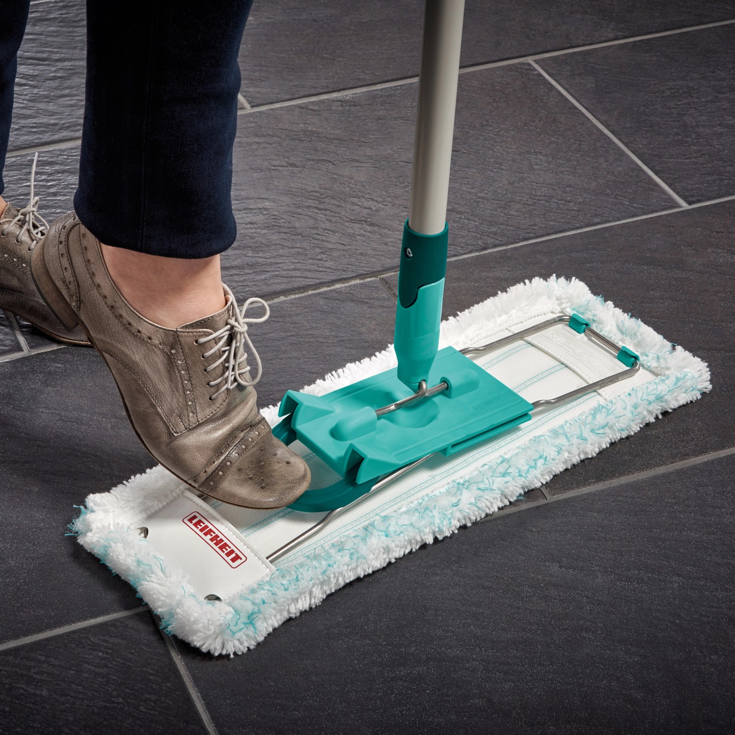 Leifheit Bodenwischer mit Fuß auf Wischtuchpresse auf dunklem Boden.