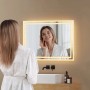 Emke Badspiegel 50x70 cm mit warmweißer LED-Beleuchtung. Frau im Bademantel betrachtet sich im modernen Badezimmer.