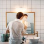 Mann rasiert sich im Bad unter einer Philips LED-Leuchtstofflampe. Spiegelschrank mit Holzrahmen und Aufsatzleuchte.