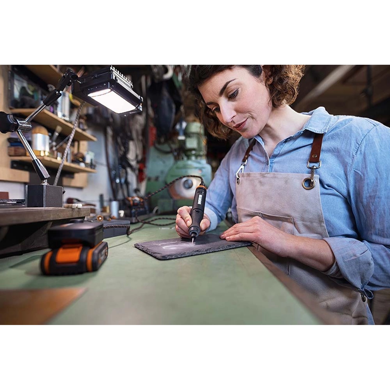 Frau graviert mit Worx MakerX Akku-Multitool ein Werkstück. Inkl. Zubehör.