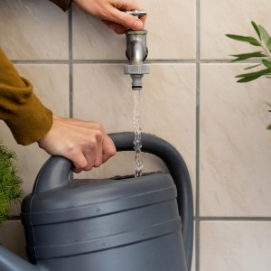 Graue Gießkanne wird mit Gardena Hahnverbinder (G 3/4) am Wasserhahn befüllt.