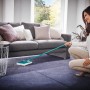Frau benutzt Leifheit Teppichkehrer Regulus zur Teppichreinigung im Wohnzimmer.