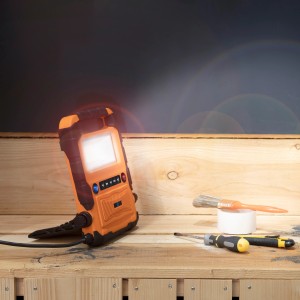Orange LED-Arbeitsleuchte mit Bluetooth Lautsprecher auf einer Werkbank.