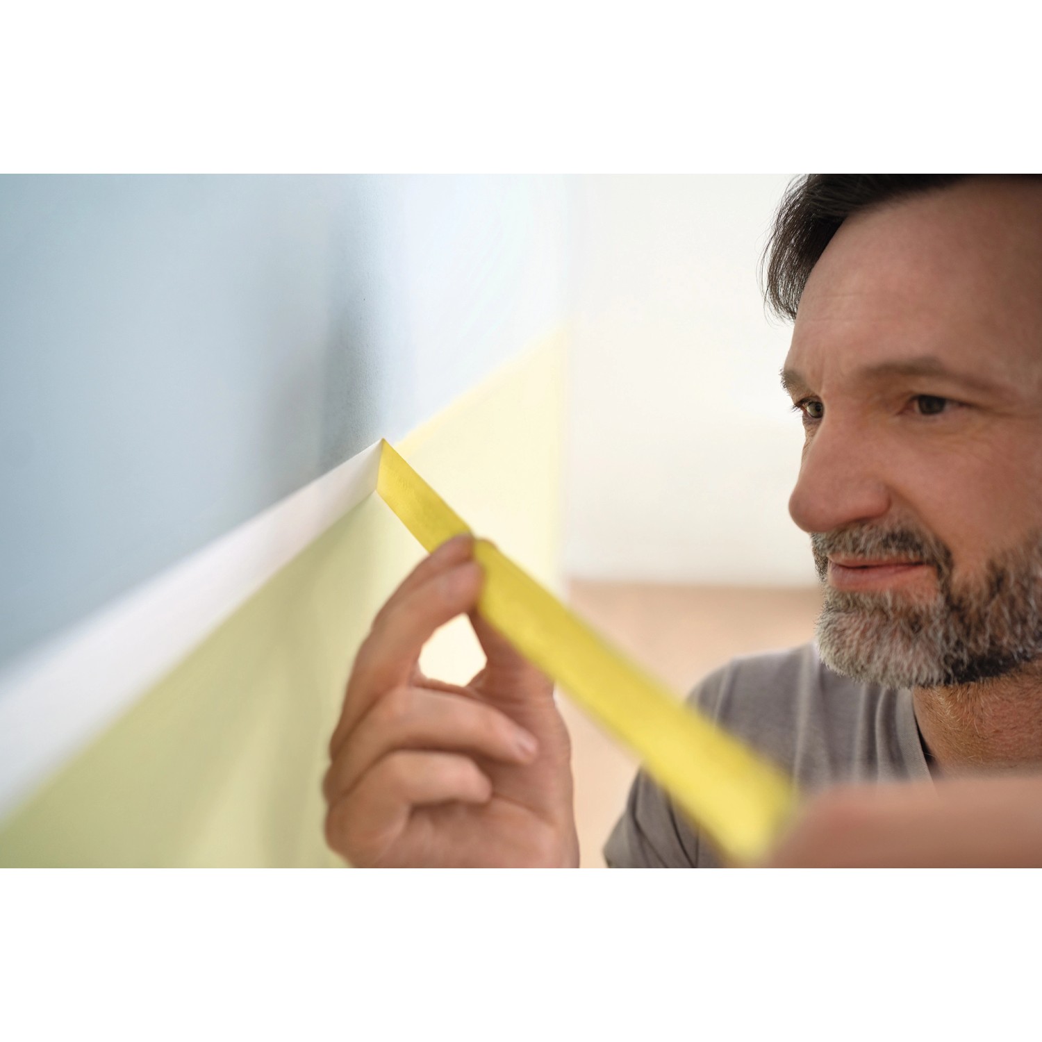 Mann klebt mit Tesa Malerband Professional eine Wand ab. Das gelbe Klebeband sorgt für scharfe Farbkanten.