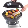 Schwarzer Holzkohle-Kugelgrill Mini mit Grillgut und Grillzange. Kompakter Grill für unterwegs.