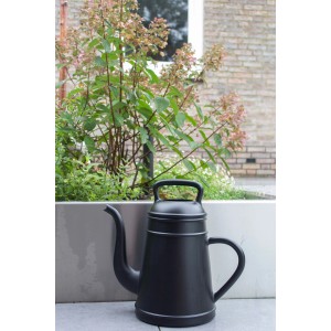 Schwarze Xala Gießkanne (8 l) vor Pflanzenkübel. Design-Gießkanne für Garten und Innenbereich.