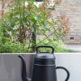 Schwarze Xala Gießkanne (8 l) vor Pflanzenkübel. Design-Gießkanne für Garten und Innenbereich.